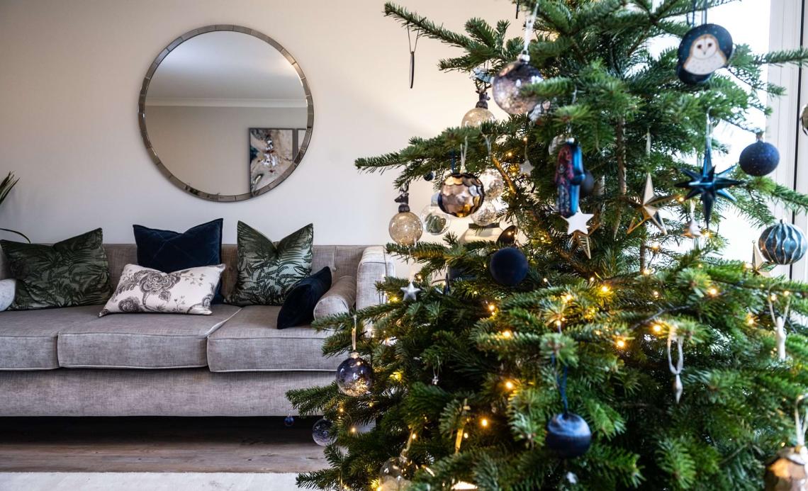 Decorated Christmas tree in a living room with a grey sofa and round mirror