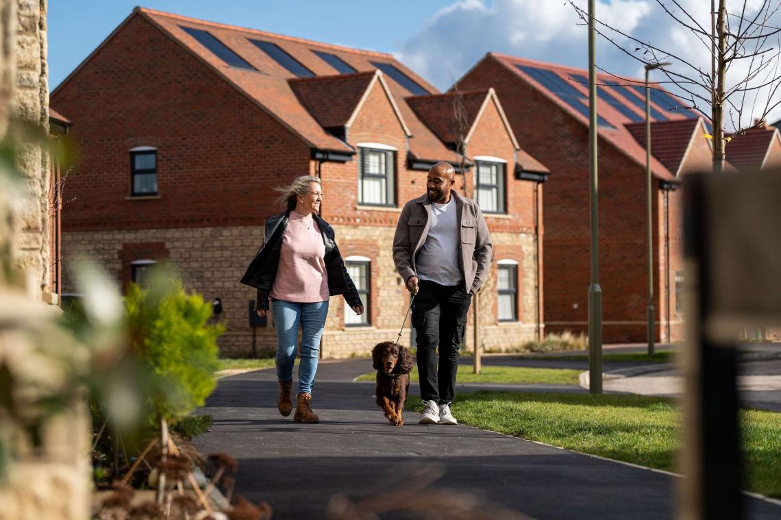 Couple walking a spaniel along a path past new brick homes with solar panels
