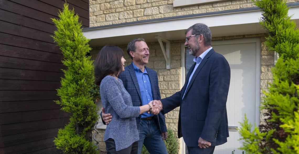 Couple shaking hands with a man outside the front door of a stone-built home