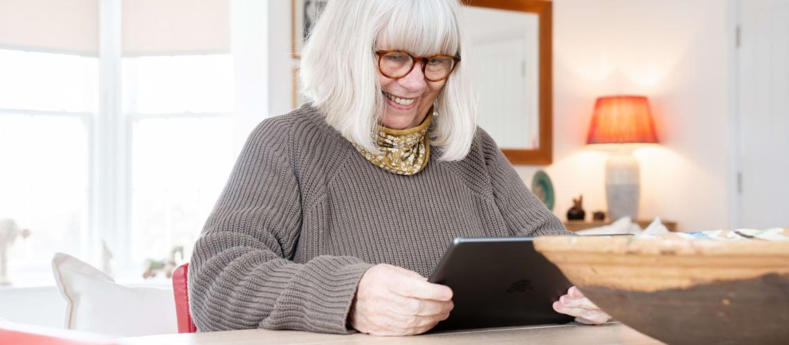 Smiling older woman using a tablet at a dining table