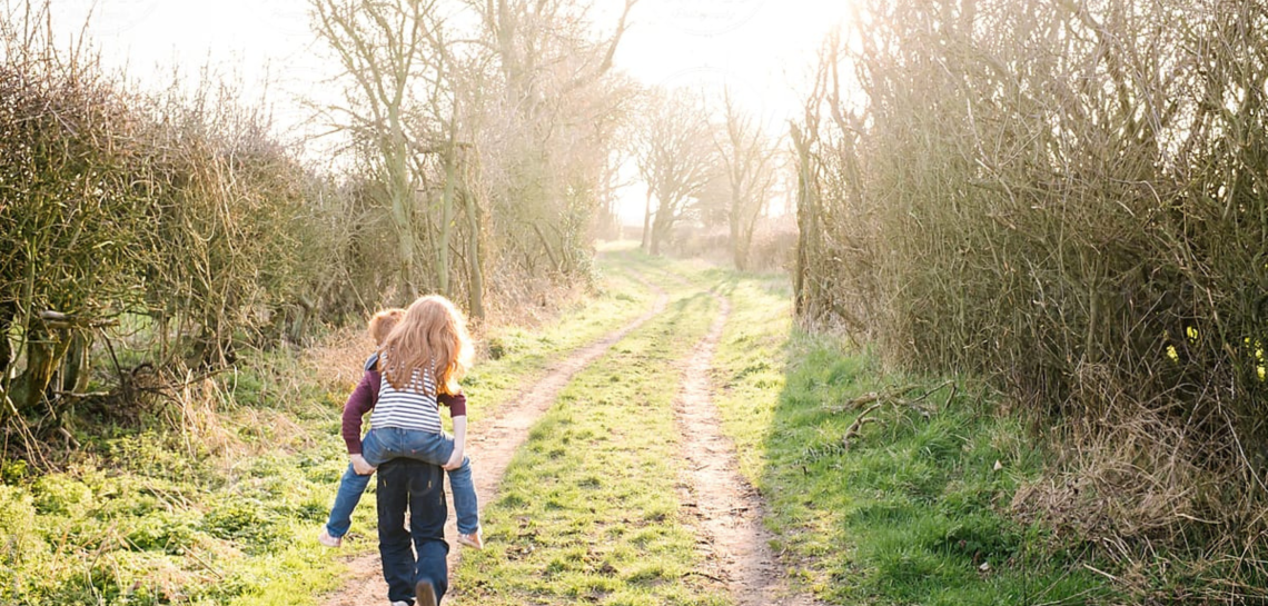 Child carrying a younger child piggyback along a sunlit country track