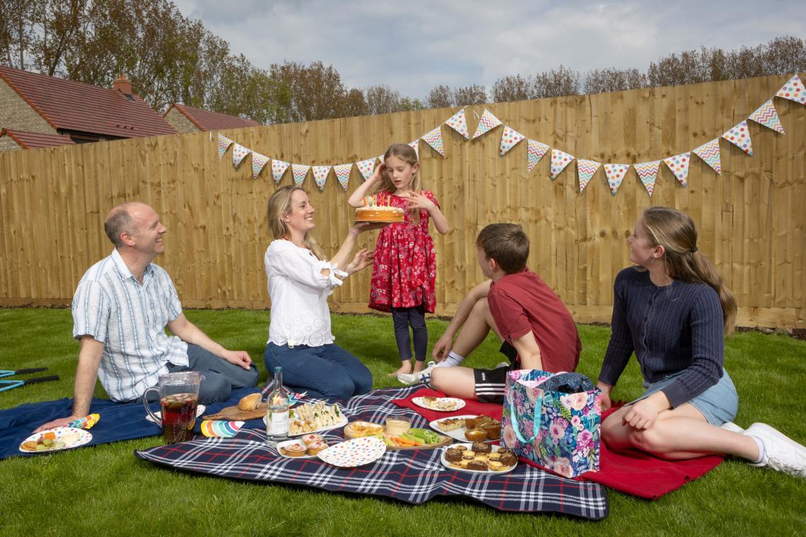 Family having a birthday picnic with cake on the lawn of their new garden