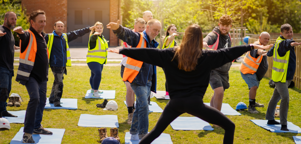 Site workers in hi-vis vests following an outdoor yoga class on mats
