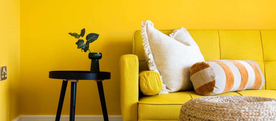 Yellow sofa with cushions beside a black side table and yellow wall