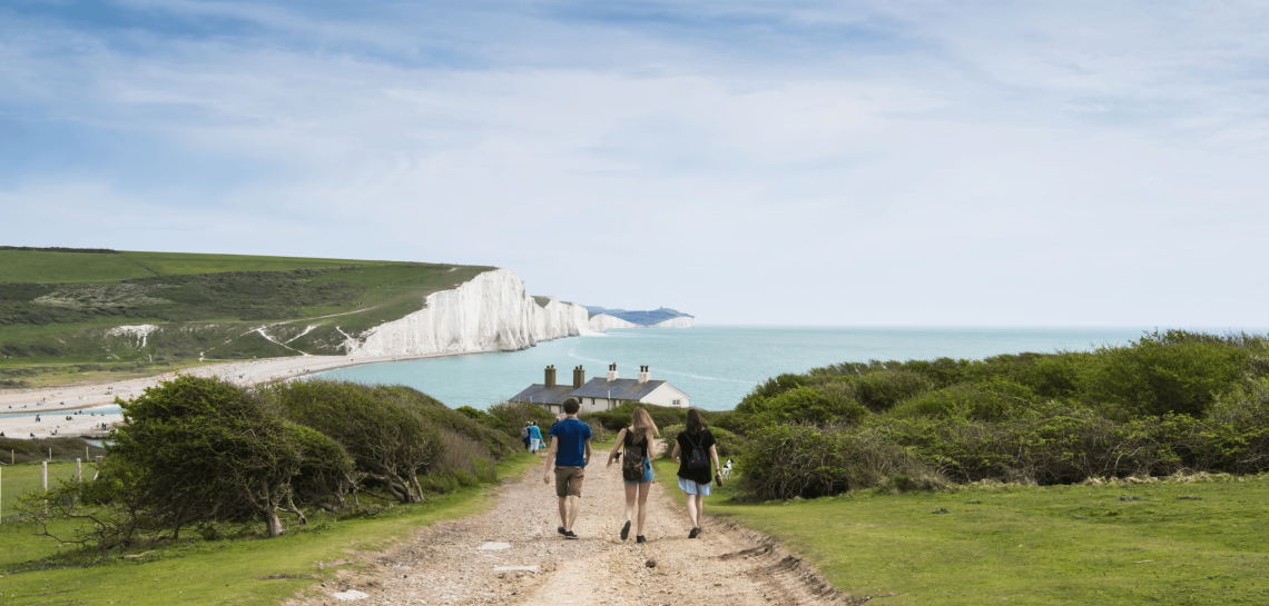 Walkers on a chalk path towards the Seven Sisters cliffs and the sea