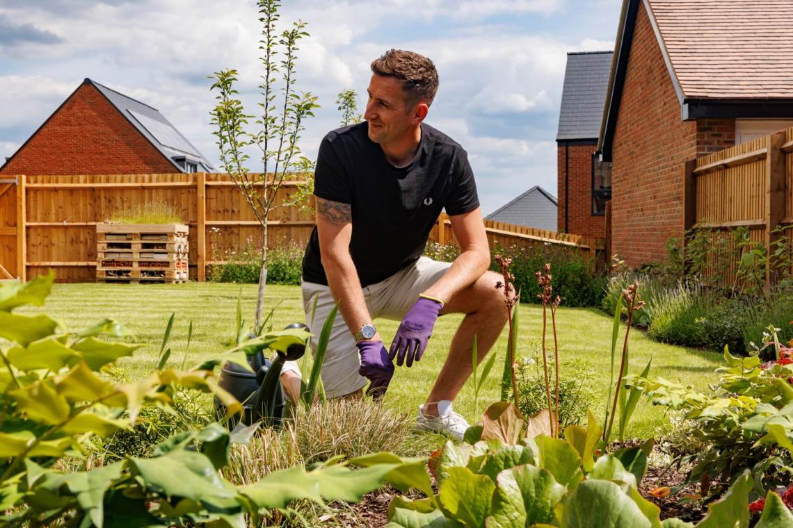 Man in gardening gloves kneeling in a planted back garden with a bug hotel at Church Farm