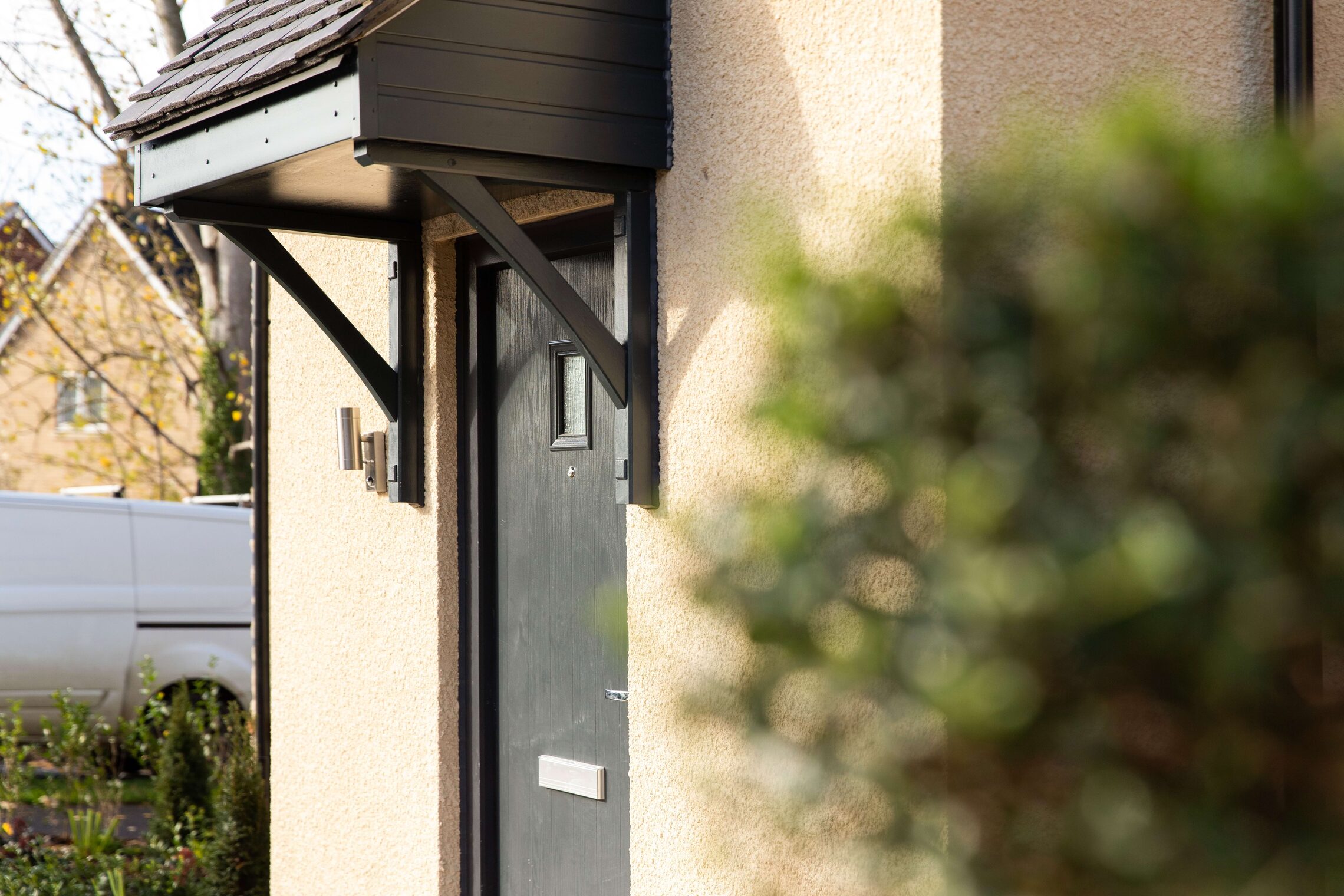 Dark grey front door with a timber canopy on a rendered house