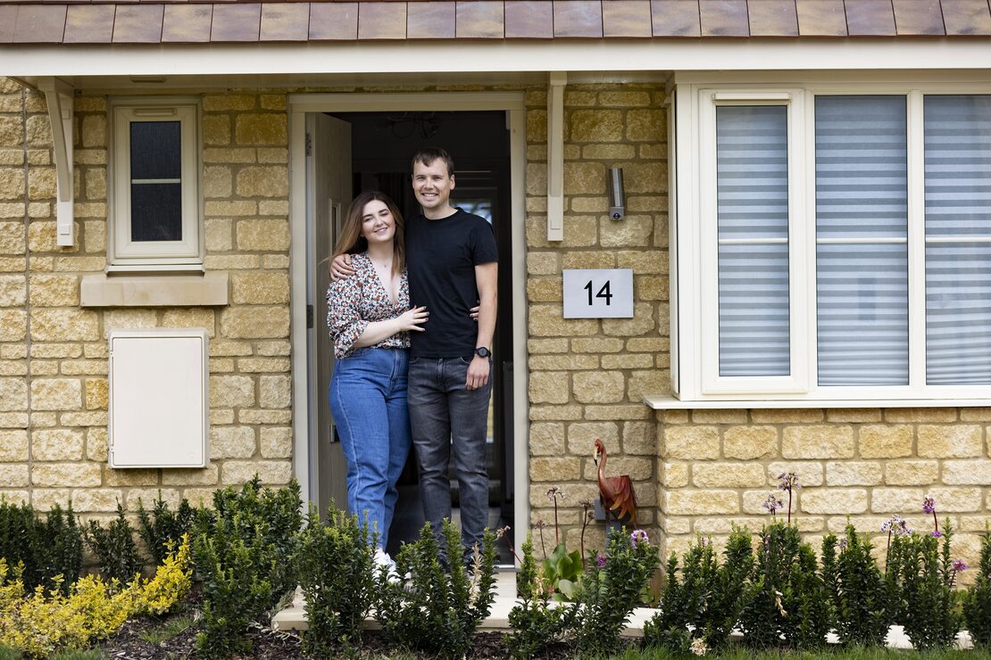 Kate and Pete, first-time buyers, at the front door of their new stone home at Hanborough Gate